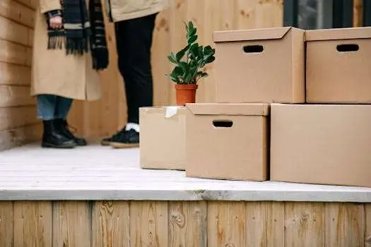 Cardboard boxes stacked on a wooden porch, symbolizing moving day with a potted plant nearby.